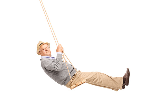 Carefree senior man swinging on a wooden swing and looking at the camera isolated on white background
