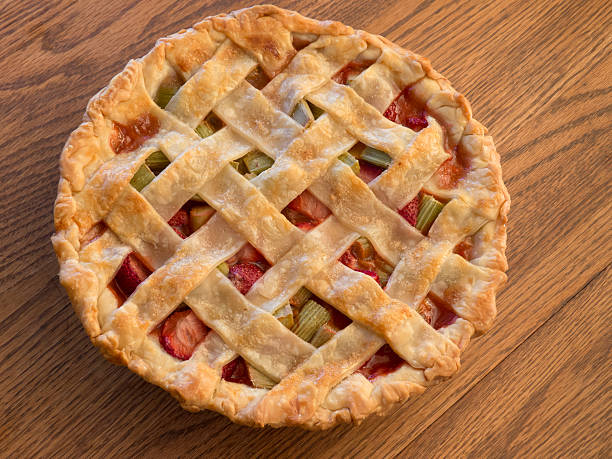 Fresh baked country style strawberry rhubarb pie with a crisscross lattice top and sprinkled with sugar on an oak tabletop.