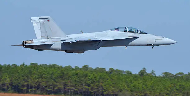 Side-view of a Navy F-18 Super Hornet fighter jet flying at tree-top level