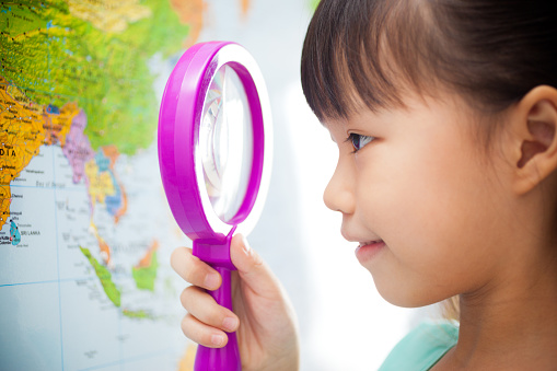 Little Chinese girl looking at a world map with magnifying glass.