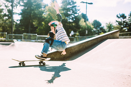 A young, elementary aged boy plays at a skate park. They boy has a helmet and padding to keep him safe as he plays and falls.  Horizontal with copy space.