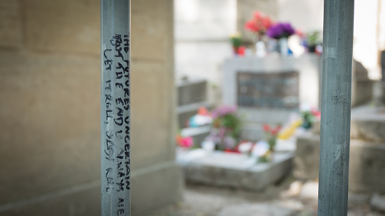 Paris, France - July 15, 2015: Jim Morrison's grave through the iron bars where the occasional tourist writes some of his most memorable verses. Selective focus on the bars.	