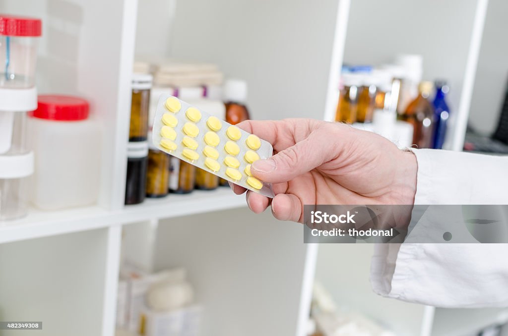 Hand holding a blister of pills Hand holding a blister of pills in front of a shelf of medical products 2015 Stock Photo
