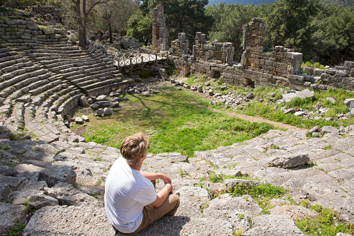 Young man sits on theatre steps of ancient Greek ruin, looks off