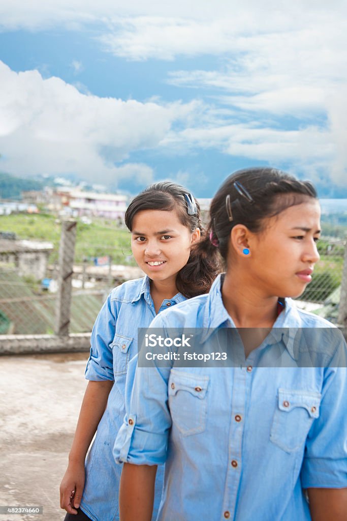 Two Asian descent, teenage girl friends hanging out. Two Asian descent, teenage girl friends hanging out together outdoors.  The happy high school students are wearing their light blue school uniforms. The city of Shillong, India can be seen in the background. Blue cloudy sky. Copyspace. Indian Ethnicity Stock Photo