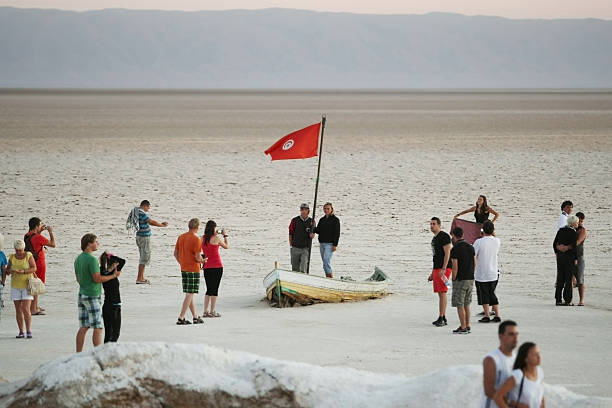 Chott El Jerid,Tunisia - September 17th, 2012 : Tourists are photographing next to an abandoned boat from which Tunisian flags is waved at Chott El Jerid, a large salt lake in southern Tunisia. Chott El Jerid is the largest salt pan of the Sahara and it can be crossed by foot.