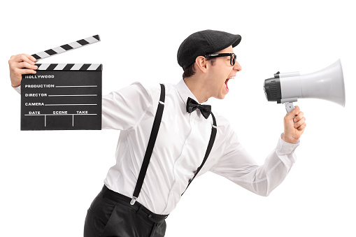 Young movie director holding a clapperboard and shouting on a megaphone isolated on white background