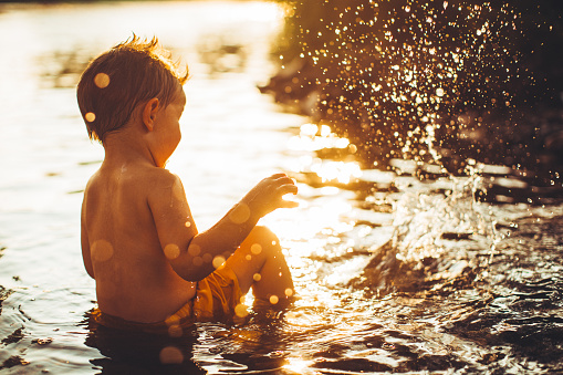 Portrait of a little boy bathing in the river, splashing and playing with water