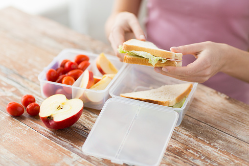 healthy eating, storage, dieting and people concept - close up of woman with food in plastic container at home kitchen