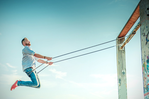 side view on smiling bearded man on swing under blue sky