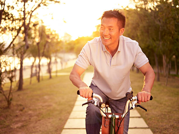 アジア人乗り自転車夕暮れ時の屋外 - mature adult vacations action adult ストックフォトと画像