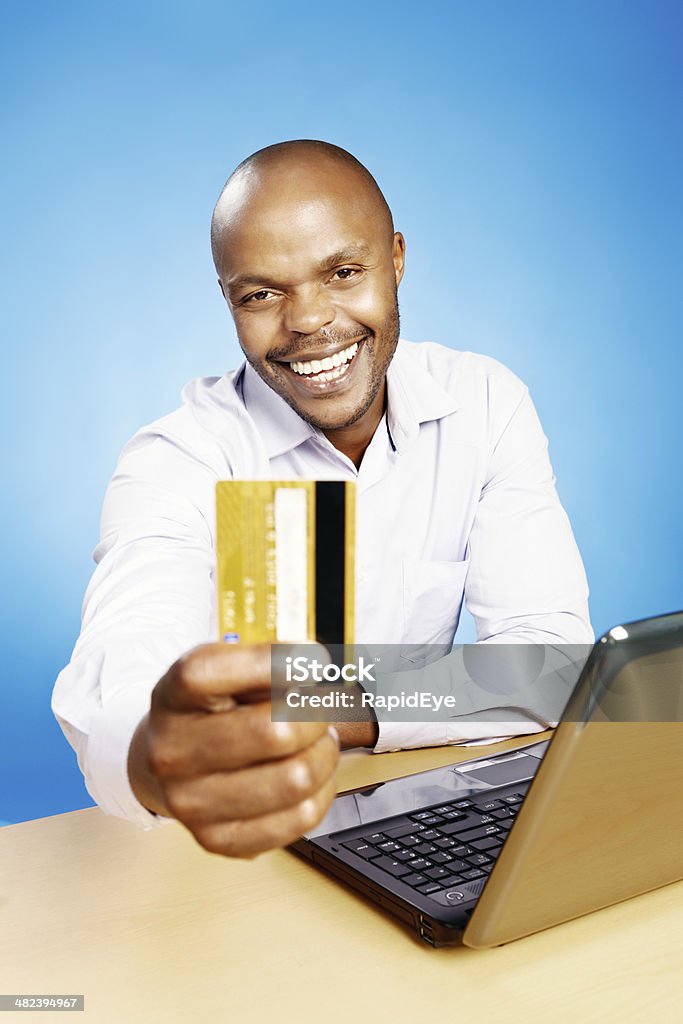 Businessman happy about e-commerce and banking shows his credit card Smiling man with open laptop holds out his credit card. He has just discovered the huge variety of goods - and services - one can buy online and the ease of internet banking. Blue background. 30-39 Years Stock Photo