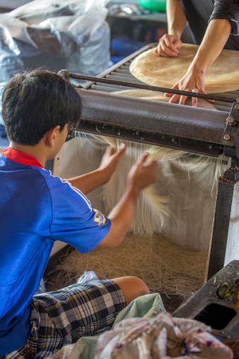 Can Tho, Vietnam - April 17, 2013: Vietnamese young man cutting rice paper to make rice noodles in a family business on the Mekong River.