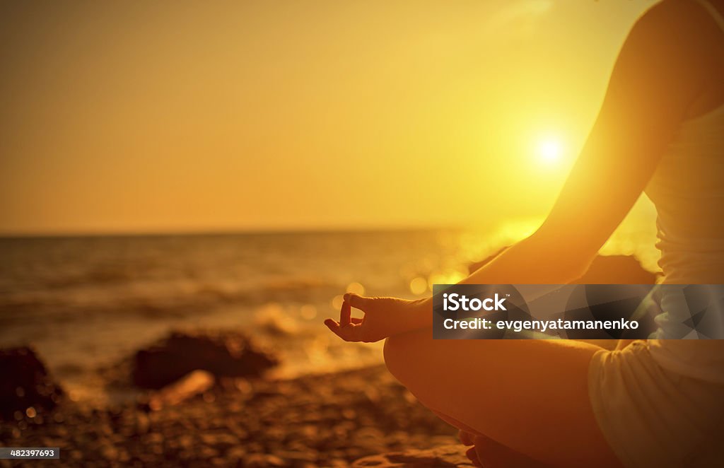 hand of  woman meditating in a yoga pose at sunset hand of a woman meditating in a yoga pose on the beach at sunset Activity Stock Photo