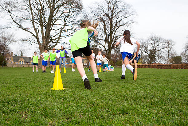Lets Get Physical School children wearing sports uniform running around cones during a physical education session. physical education stock pictures, royalty-free photos & images