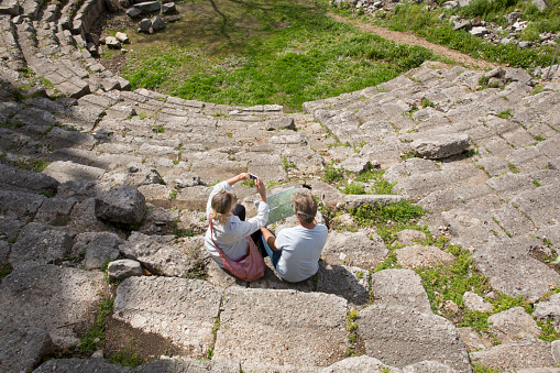 Couple sit on theatre steps of ancient Greek ruin, look at map