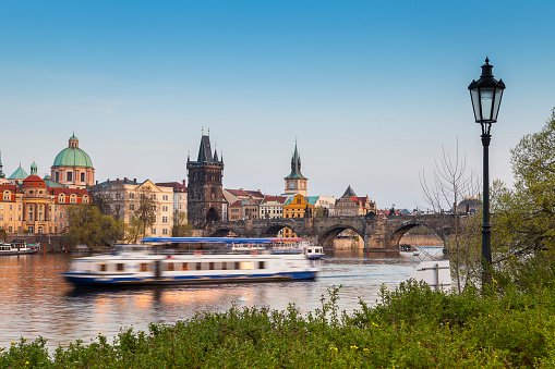 A boat cruises along down the river in Prague, with clear blue skies and beautiful buildings.