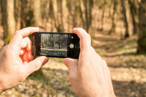 Bad Oeynhausen, Germany - March 29, 2014: Guy is taking a photo with his iPhone in a sunny forrest. photographing with mobile phones becomes more and more in common. A typical scene you can see everyday.
