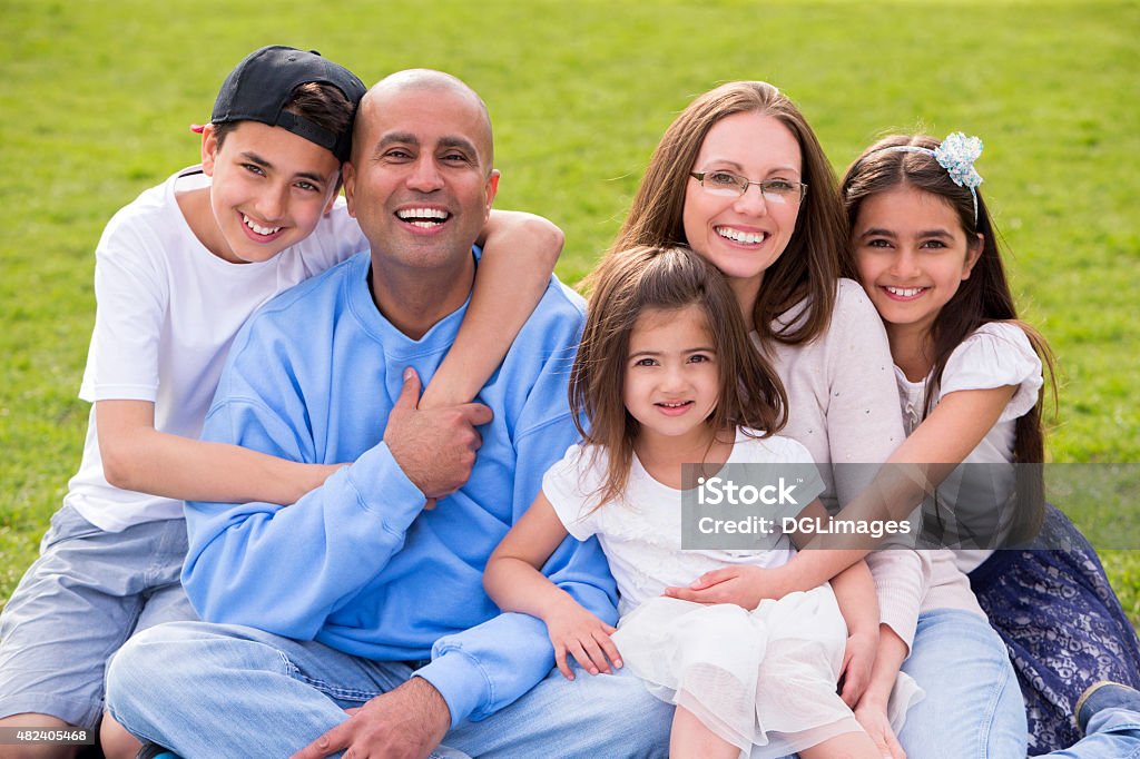 Happy Family A portrait of a mixed ethnicity family, mum and dad have three cute children between the ages of 4 to 10. They are sitting down and smiling happily at the camera. 2015 Stock Photo