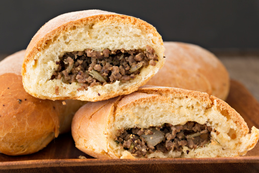A close up shot of baked piroshki with one cut in half to reveal the beef filling inside.