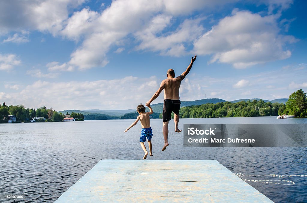 Father and son jumping in lake Father and son jumping in lake Sept-Iles (Portneuf) from the dock Jumping Stock Photo