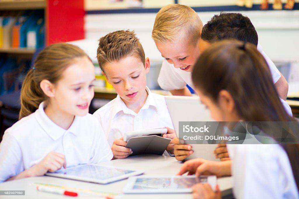 Friends in the Classroom Happy students in classroom using a digital tablet, they are all wearing uniforms. Child Stock Photo