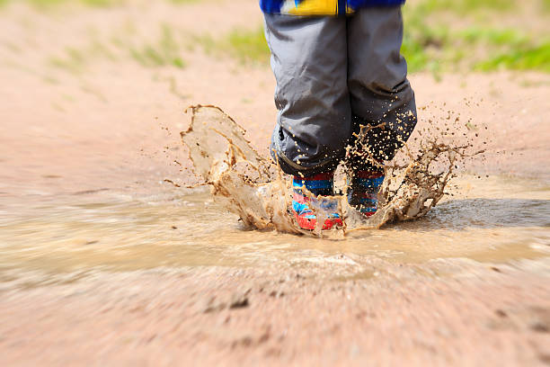 istock Child wearing red rain boots jumping into a puddle 482408060