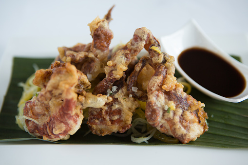 Soft shell crab on a bed of mango, cucumber salad and soy sauce dip served on a white plate.