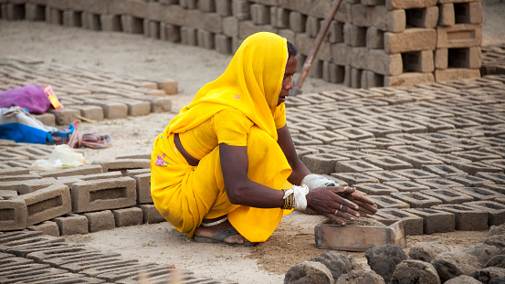 Bhandavgarh, India - February 3, 2013: Woman, part of an rural scnene in the open field, making bricks using a mold and clay.