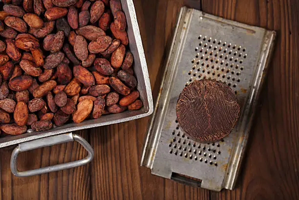 roasted cocoa beans in Vintage heavy cast aluminum roasting pan and and 100% solid chocolate on wood background