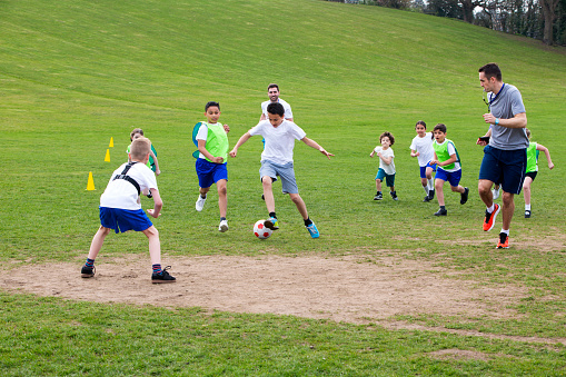 Adults on grassed area with school children supervising a soccer game, Everyone can be seen running and chasing the ball.