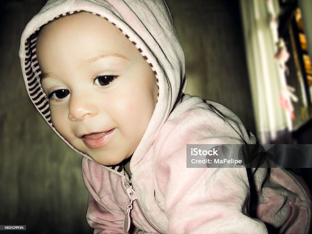 Close-up Portrait of Smiling 10 Month Old Baby Wearing Hood A close-up photo of a caucasian 10 month old girl smiling. She is wearing a pink sweatshirt and hood. She is lit by a strobe positioned in front of her and the backgroud is lit by a soft light coming from the window. 2015 Stock Photo