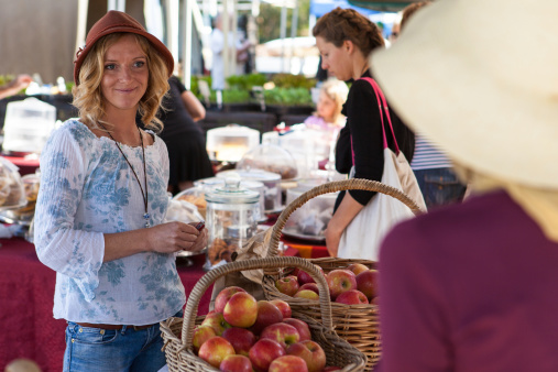 Byron Bay, New South Wales, Australia – September 27, 2012: Young woman selling apples at Byron Bay farmer's market