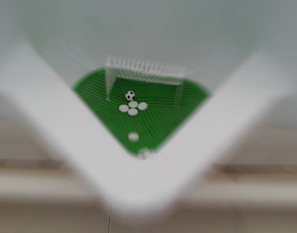 Interior of a public male restroom in dark gray tones. Original urinal with miniature football goal and ball. WC for football fans. Top view
