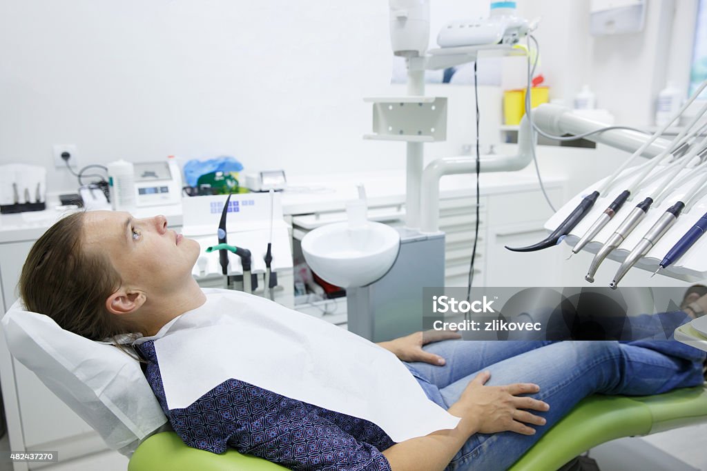Patient sitting on dental chair Patient sitting on dental chair wearing dental bib, waiting for her dentist. Dental medicine, dental care, prevention, health concept. Anxiety Stock Photo