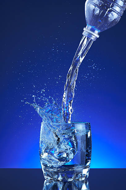 botella de agua que pours de agua en un vaso sobre un fondo azul - water flowing water pouring ice fotografías e imágenes de stock