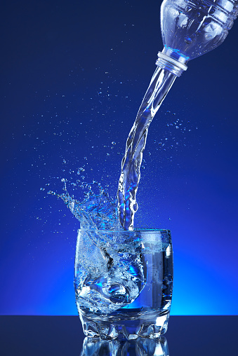 Water poured into a glass, splash, blue background, refreshing, freshness and health. Water bottle, water pitcher, blue liquid, ice, drops, motion, wave, splash, transparent blue water,