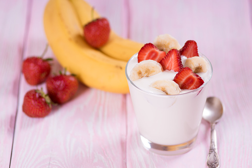 Yogurt with strawberries and banana in a glass. Pink background.