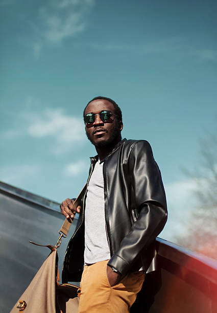 Fashion elegant young african man wearing a black leather jacket with bag in the city over evening sky