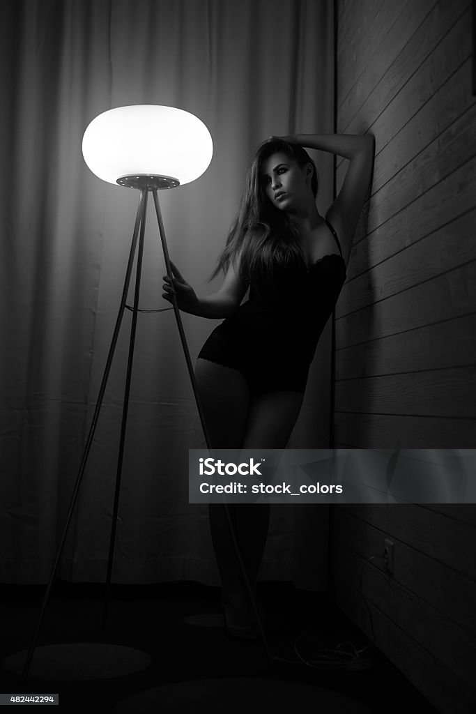 the beauty is waiting for you black and white shot of attractive woman in black lingerie posing in bedroom near light, holding hand in head. 2015 Stock Photo