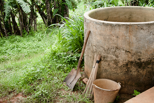 Old well on a pig farm in Meghalaya, India. A crude shovel, broom and pail are beside the well. Jungle type climate in background. Empty, no people.  Copyspace.