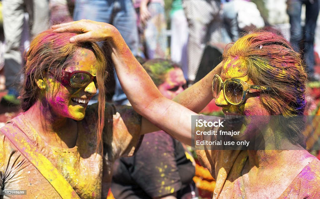 Holi Festival Jaipur, India - March 17, 2014: Two girl with sunglesses who covered with paint are throwing colored powder to each other's heads at the Holi Festival. Holi is a spring festival also known as the festival of colours and the festival of love. Holi festival has an ancient origin and celebrates the triumph of 'good' over 'bad'. The colorful festival bridges the social gap and renew sweet relationships. On this day, people hug and wish each other 'Happy Holi'. People spend the day smearing and throwing colored powder all over eachother's faces-bodies, having parties and dancing. Photo was taken in public area. Holi Stock Photo