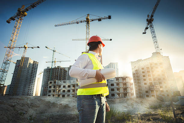 istock Man in hardhat and green jacket posing on building site 482453504
