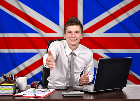 businessman sitting in office and reaches out on a british flag on background