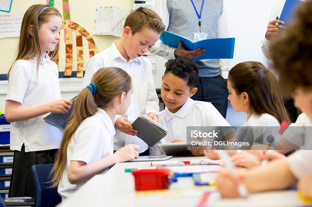 Happy at School A group of school children can be seen working on digital tablets and whiteboards, they are all working happily. Two unrecognisable teachers can be seen in the background. School Children Stock Photo