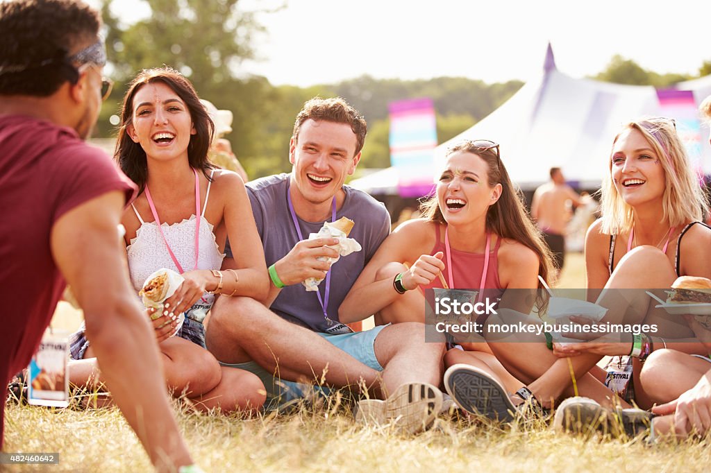 Friends sitting on grass and eating at music festival Music Festival Stock Photo