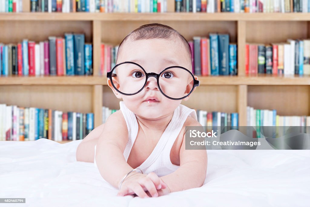 Sweet baby with glasses and a bookcase background Lovely male infant wearing glasses and looking at the camera, shot with a bookshelf background Baby - Human Age Stock Photo
