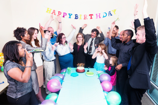This is a horizontal, color photograph of an office party celebrating a co-worker's birthday. 