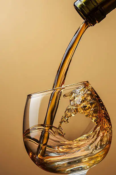 Cognac pouring from bottle into glass with splash on brown background