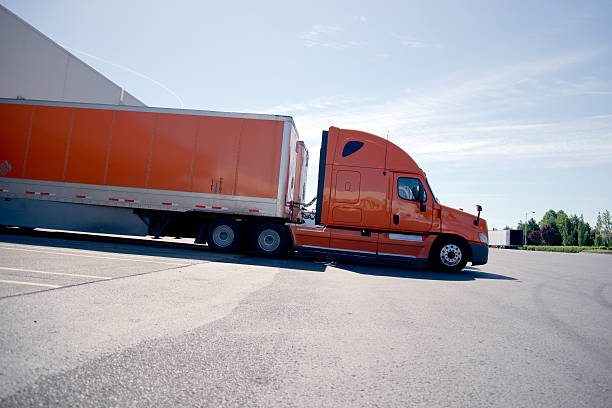 istock Orange stylish semi truck trailer unloading cargo in warehouse 482471256